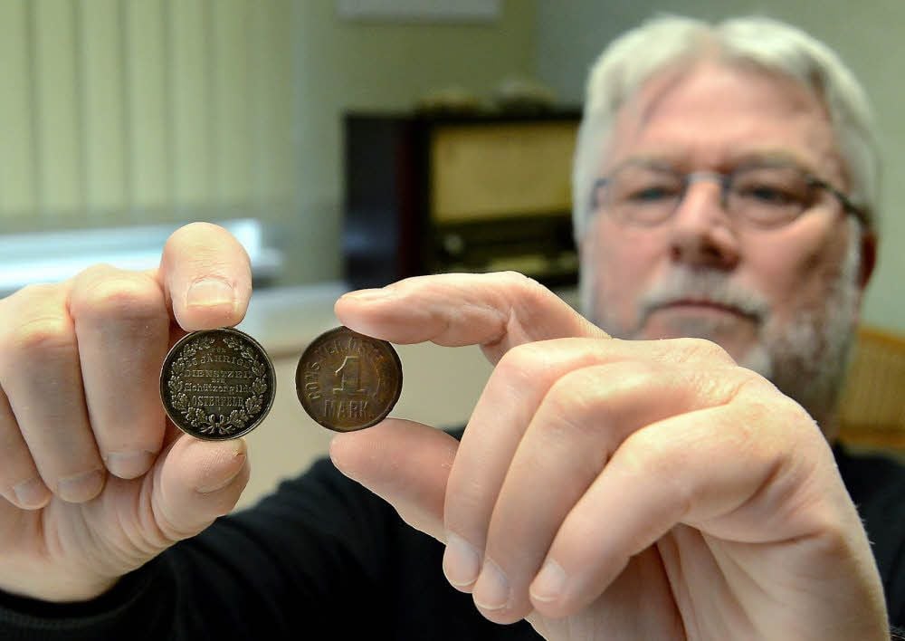 Der Vorsitzende Gerd Seidel zeigt ein altes Geldstück - vermutlich aus dem Jahr 1917 (re.) - und eine Silbermedaille vom Osterfelder Schützenverein.