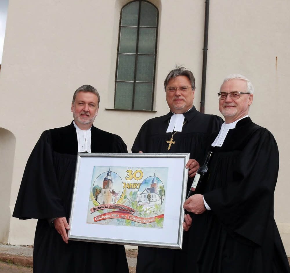 Gröbzigs Pfarrer Tobias Wessel (links) und Kirchenpräsident Joachim Liebig überreichen ein Bild über das Jubiläum der Partnerschaft an den Göllheimer Pfarrer Peter Rummer (rechts).