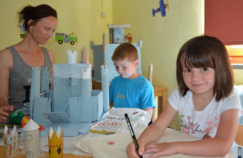 Pauline schreibt ihren Namen auf einen Stoffbeutel. Leiterin Melanie Krzebek hat mit Luca aus Altpapier ein Schloss gebaut.