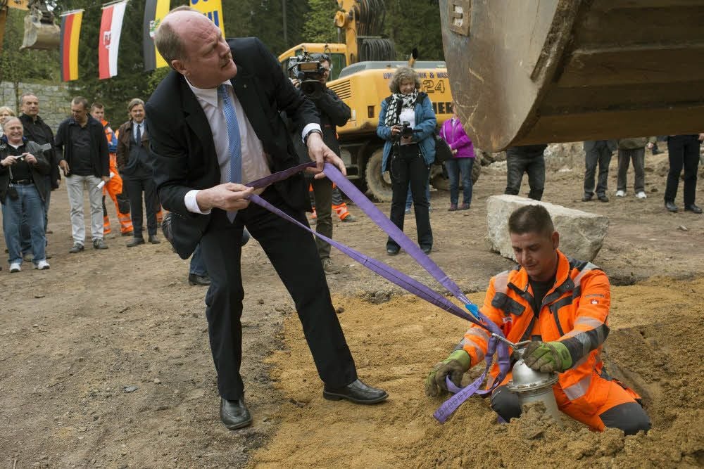 Minister Thomas Webel geht dem Baumaschinisten Dirk Sallier zur Hand, damit die Plombe ins Loch gehoben werden kann.