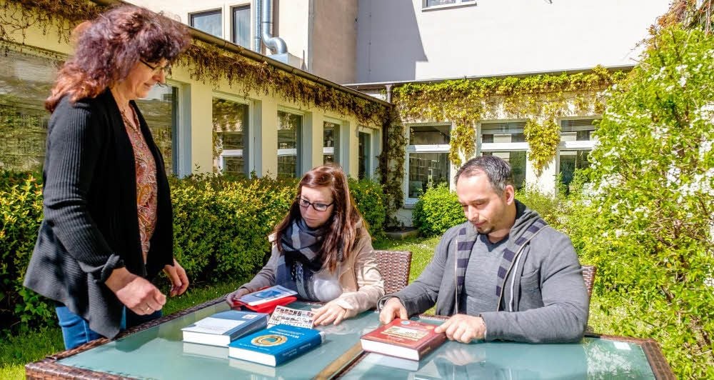 Neue Ideen für mehr Besucher der Stadtbibliothek: Bibliotheksleiterin Kathrin Hanß (l.) bringt Thomas Krause und Stephanie Präger Ausleihbücher zum Lesen in den grünen Innenhof. In der "Oase der Stille" kann seit neuestem geschmökert werden.