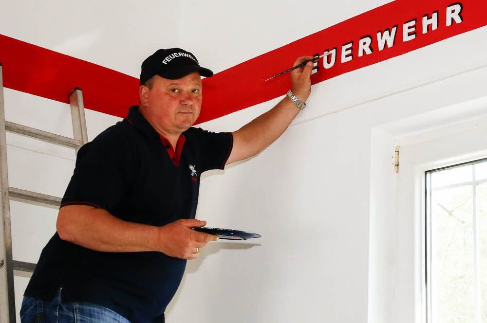Wehrleiter Olaf Nimmoth legt selbst mit Hand an und hilft beim Malern im Gerätehaus mit. Ein neuer Schriftzug ziert nun den Raum.