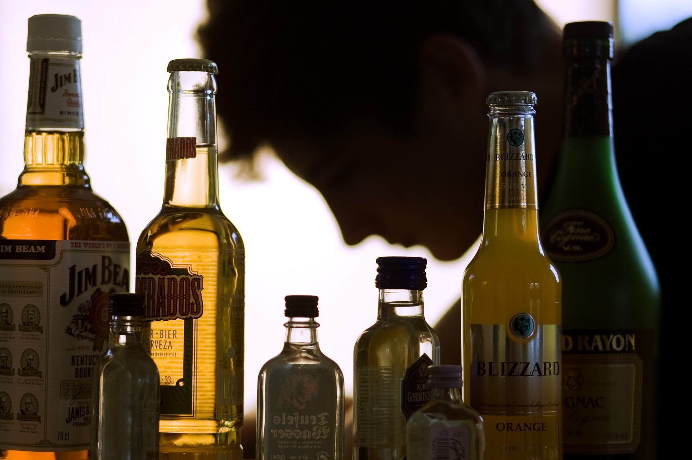 Ein Jugendlicher sitzt hinter zahlreichen Flaschen mit Alkohol.