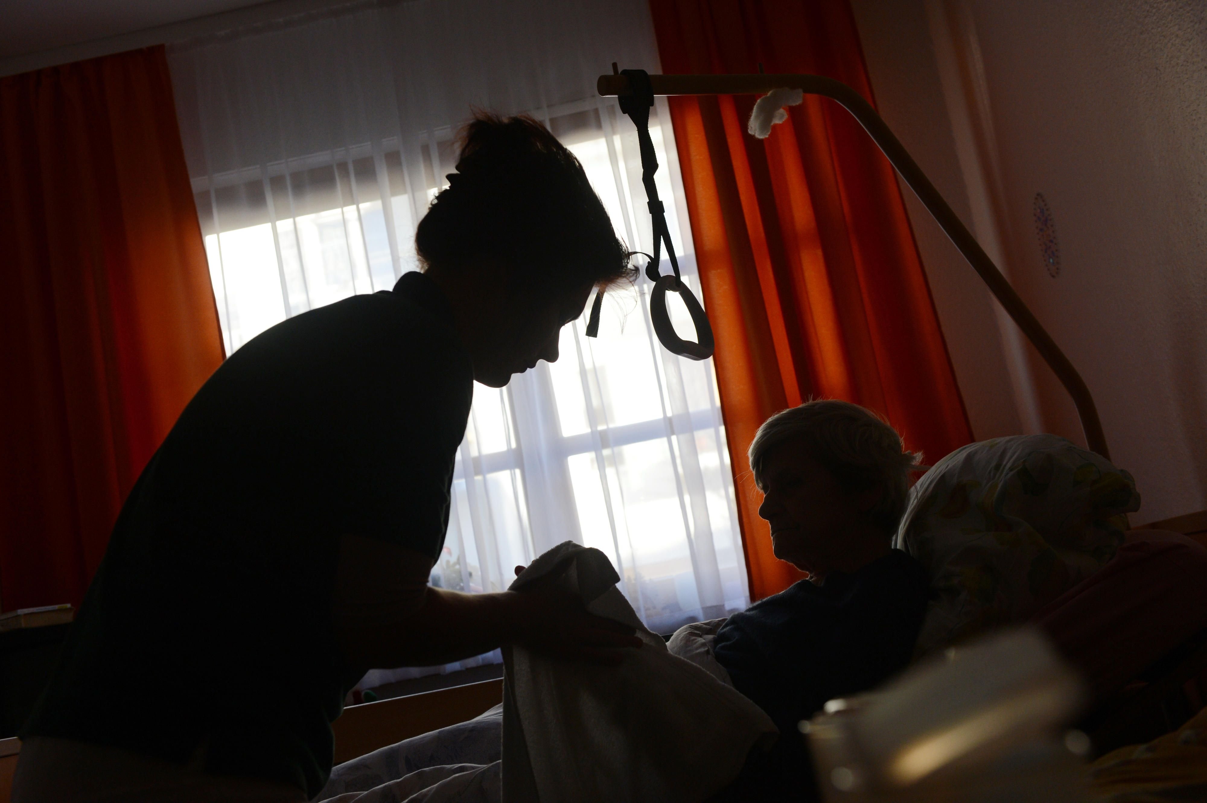 Eine Frau wird in einem Seniorenpflegeheim in ihrem Bett in ihrem Zimmer von einer Pflegerin betreut.