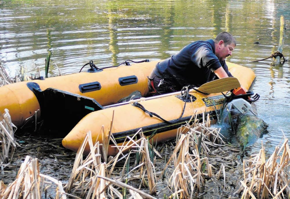 Von einem Schlauchboot aus erreicht Jörg Hesse mit der Kettensäge Bäume im Wasser, die zu weit entfernt vom Ufer liegen.