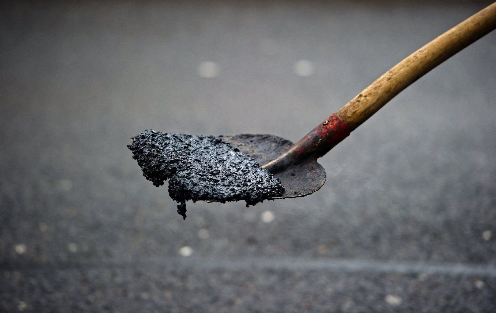 Ein Straßenbauarbeiter hält eine Schaufel mit Asphaltmasse.
