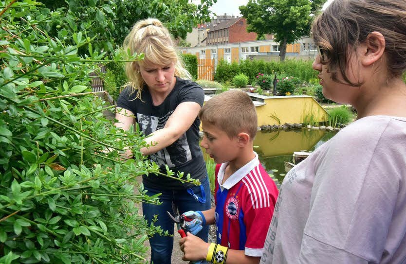 Schulsozialarbeiterin Kristin Scharf weist Sebastian Tischer in seine Aufgabe ein - Hecke verschneiden. Er ist mit Eifer bei der Sache.