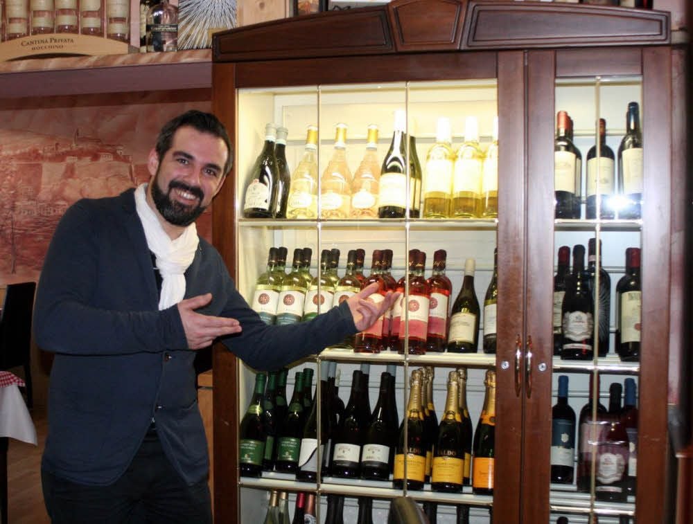 Arben Jusufi macht hier mit einer absichtlich theatralischen Geste auf das reichhaltige Angebot an Weinen aufmerksam, die sich die Gäste im „Al Dente“ in Jessen munden lassen können.
