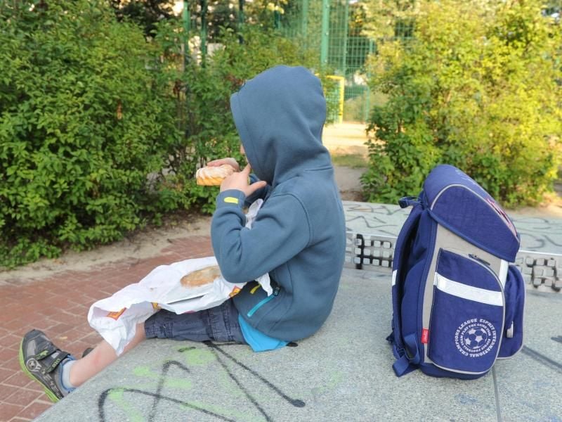 Ein Kind sitzt mit seinem Schulranzen und Kuchen auf einer Tischtennisplatte auf einem Spielplatz. Foto: Jens Kalaene