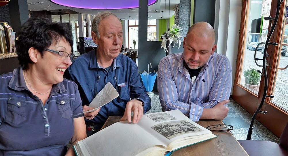 Christel und Harald Küster blättern gemeinsam mit Sohn und Nachfolger Veit im Fotoalbum.