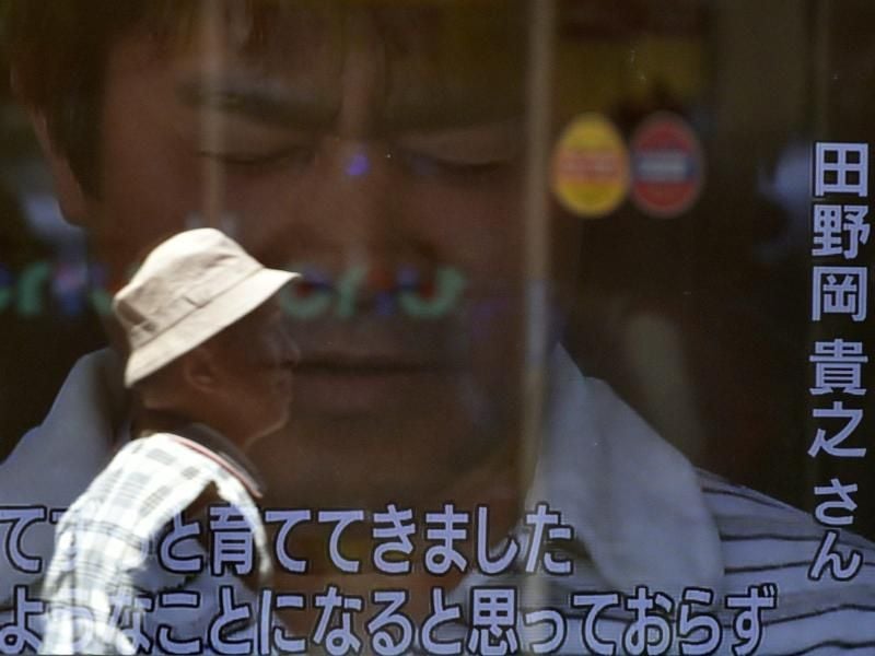 Reflexion eines Fußgängers auf einem Fernsehbildschirm, mit dem reumütigen Vater des Siebenjährigen japanischen Jungen. Foto: Franck Robichon