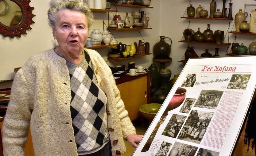Anna Goschala mit einer Tafel, auf der der berufliche Start ihres Mannes in einer Bürgeler Töpferei dargestellt ist.