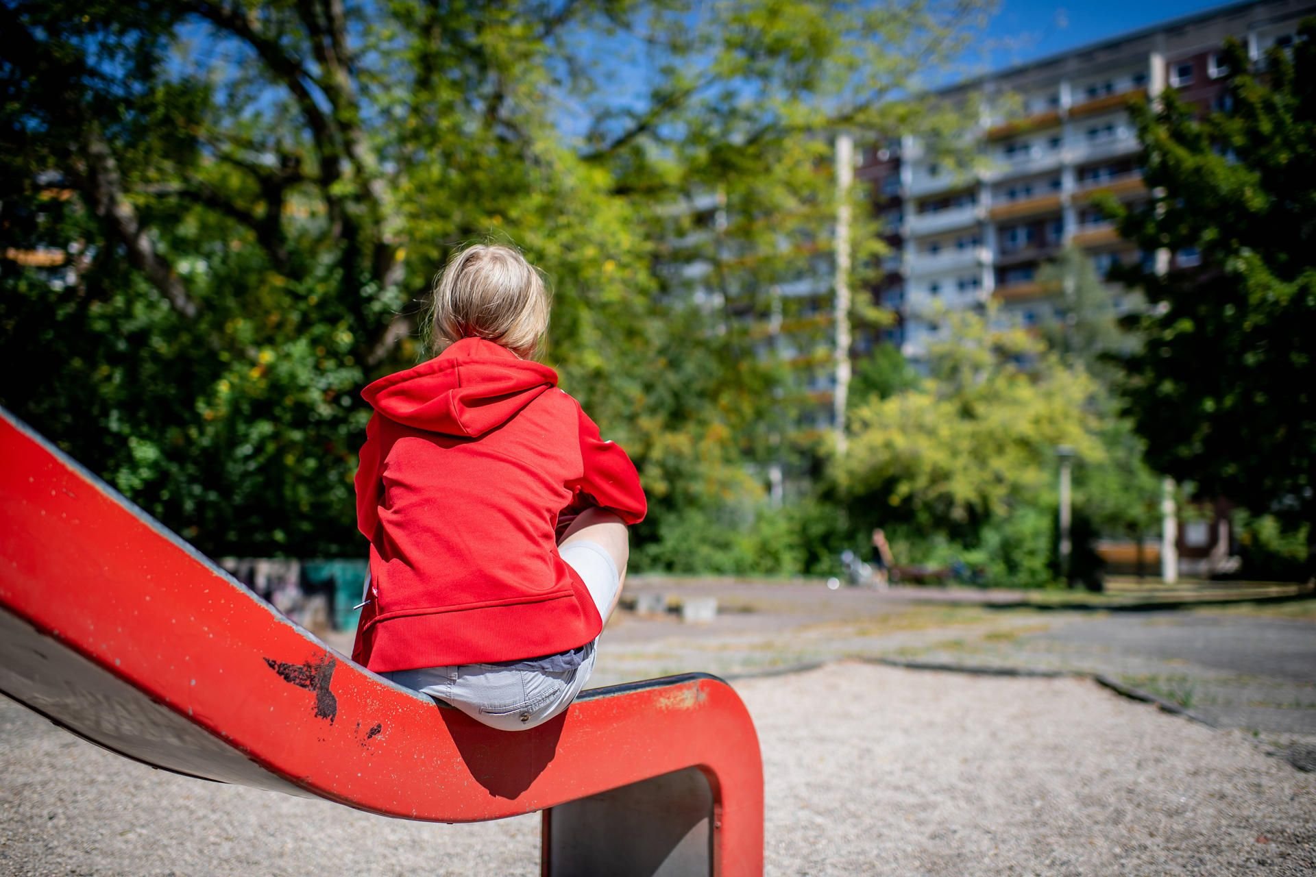 Ein Kind sitzt auf einem Spielplatz vor einem Plattenbau.
