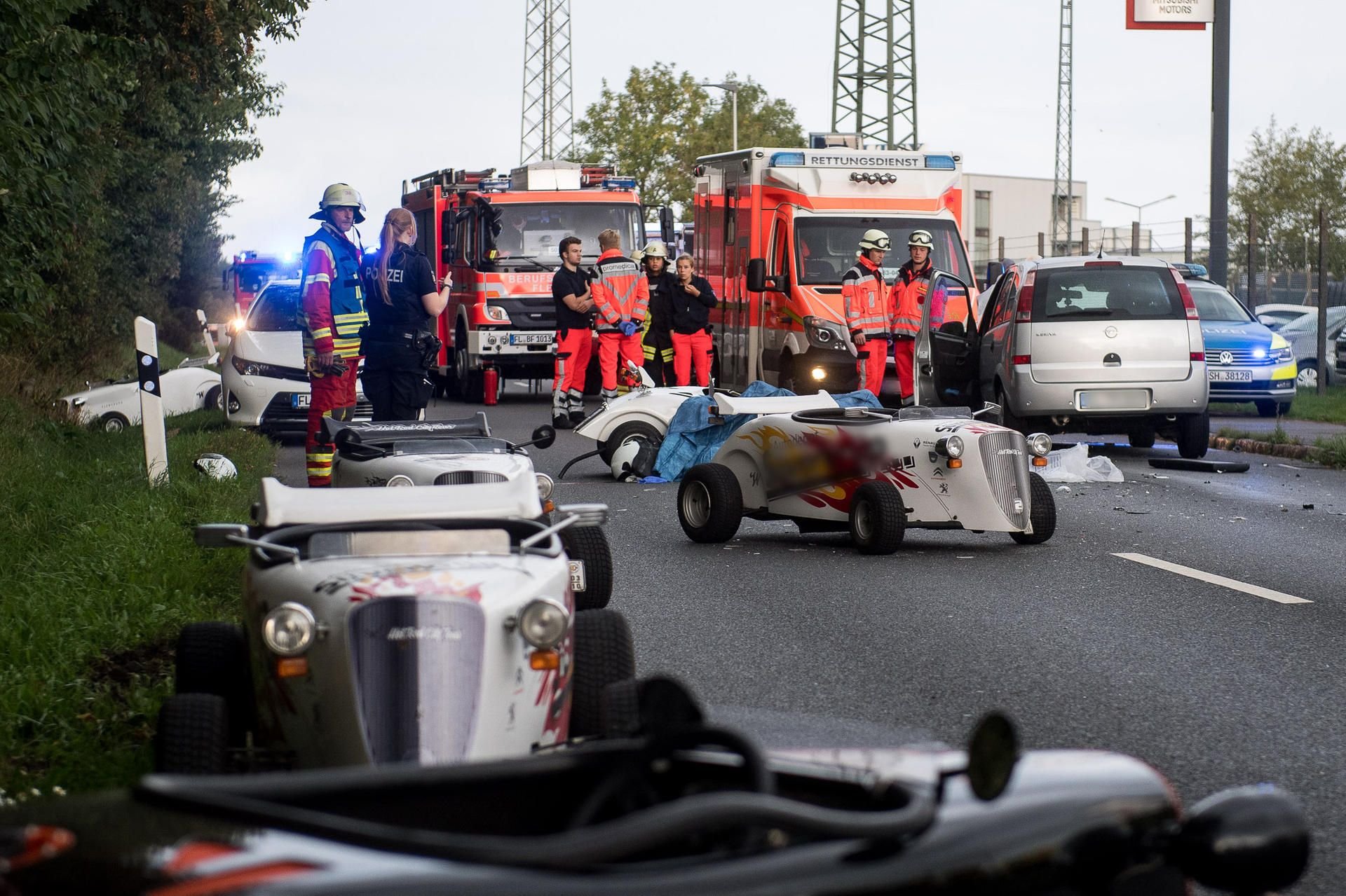Mehrere Mini-Hot-Rods und ein beschädigtes Auto stehen auf einer Straße in Flensburg. Der Fahrer eines der kleinen Fahrzeuge starb noch am Unfallort.