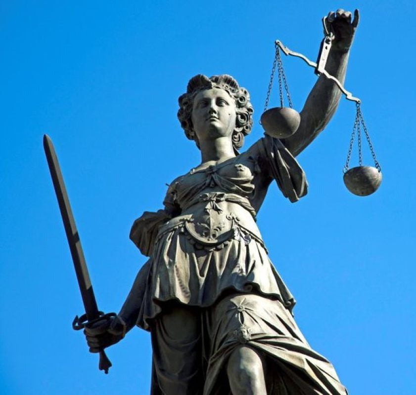 Statue der Justitia: Augenbinde, Waage und Richtschwert symbolisieren Rechtssprechung ohne Ansehen der Person, sorgfältige Abwägung und nötige Härte.