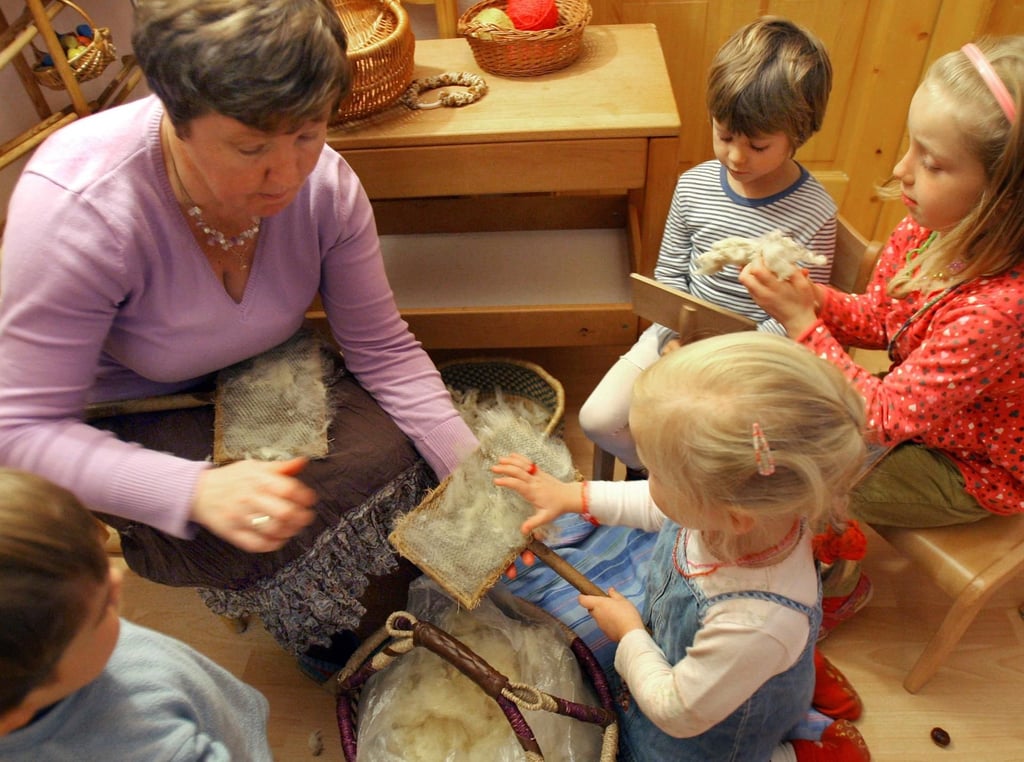 In der Kindereinrichtung „Unterm Regenbogen“ in Halle (Saale) probieren die Kinder Milan, Filine, Charlotte, und Anastasia mit Luba Balde (v.l.), wie Wolle gekämmt werden kann.
