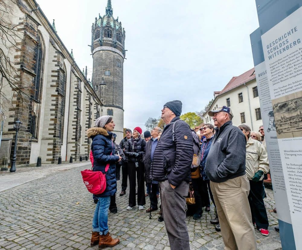 Eine Touristengruppe aus Amerika an der Schlosskirche, geführt von Katja Köhler. Ganz in der Nähe ist die Tourist-Information Wittenberg zu finden.