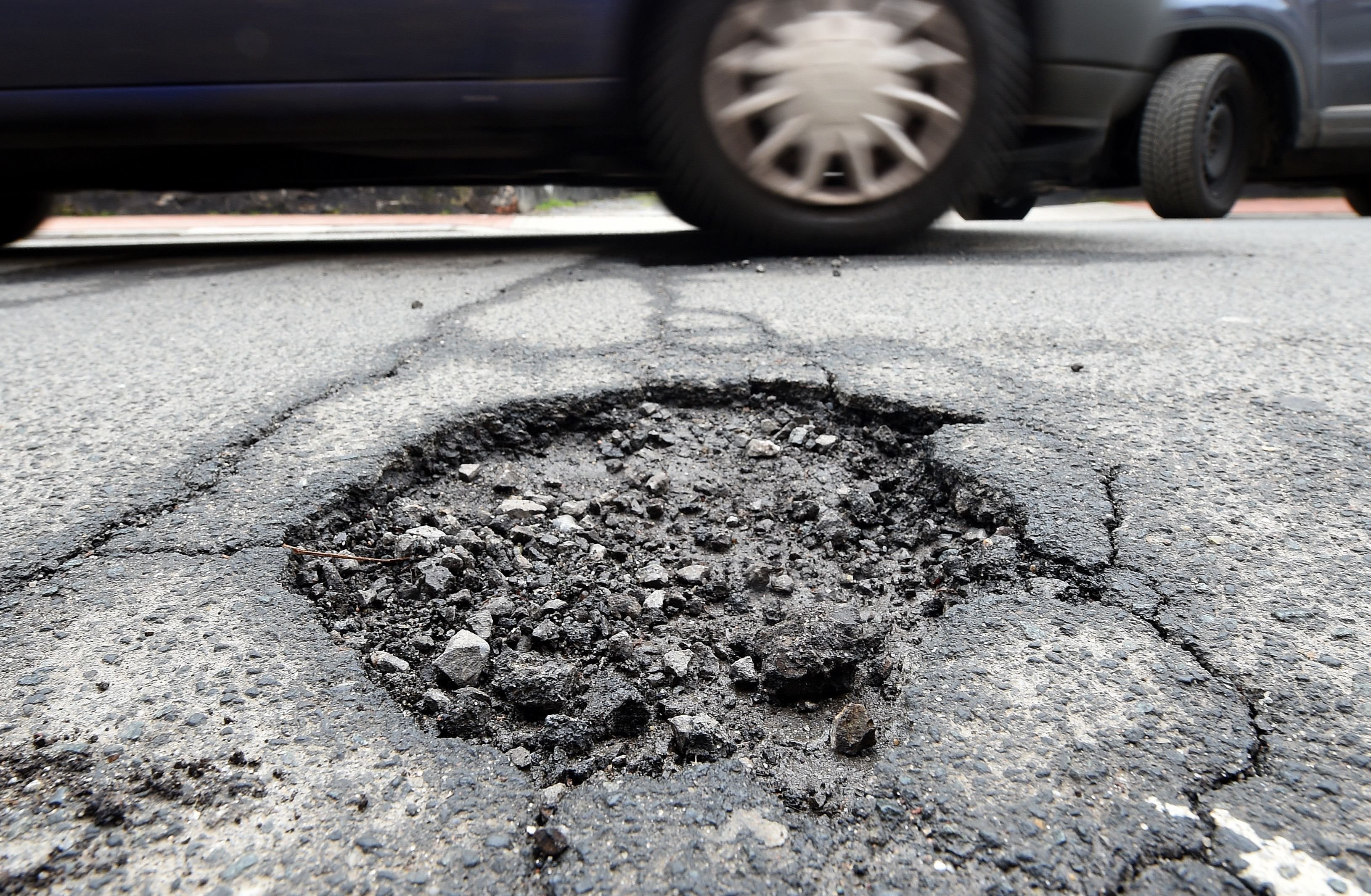 Ein Fahrzeug befährt eine Straße mit beschädigtem Asphalt.