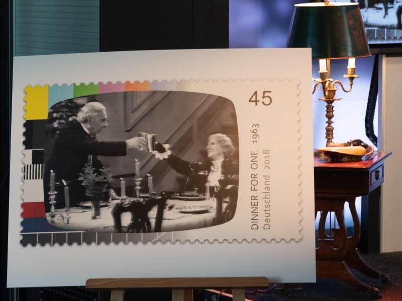 Ein Bild der Sonderbriefmarke "Dinner for One" steht auf einer Staffellei vor dem Ambiente der Fernsehproduktion. Foto: Axel Heimken/aktuell
