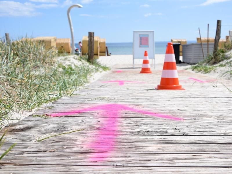Auf den Boden gesprühte Pfeile und Pylonen regeln den Zugang zum Strand in Haffkrug. Foto: Daniel Bockwoldt/dpa/Archivbild