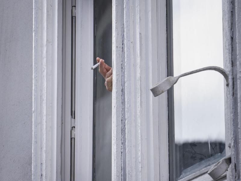 Ein Mann raucht während der Ausgangsbeschränkung am Fenster. Foto: Frank Rumpenhorst/dpa