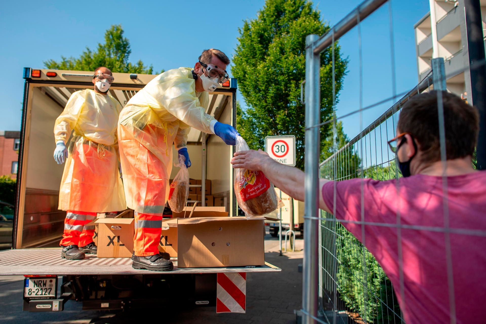 Helfer des Roten Kreuzes tragen Mundschutz und Schutzkleidung, während sie Brot an Bewohner eines Wohnhauses verteilen, das unter Quarantäne gestellt worden ist. Die Stadt Verl hat nach positiven Corona-Tests bei zahlreichen Tönnies-Mitarbeitern im Stadtteil Sürenheide eine Quarantäne eingerichtet.
