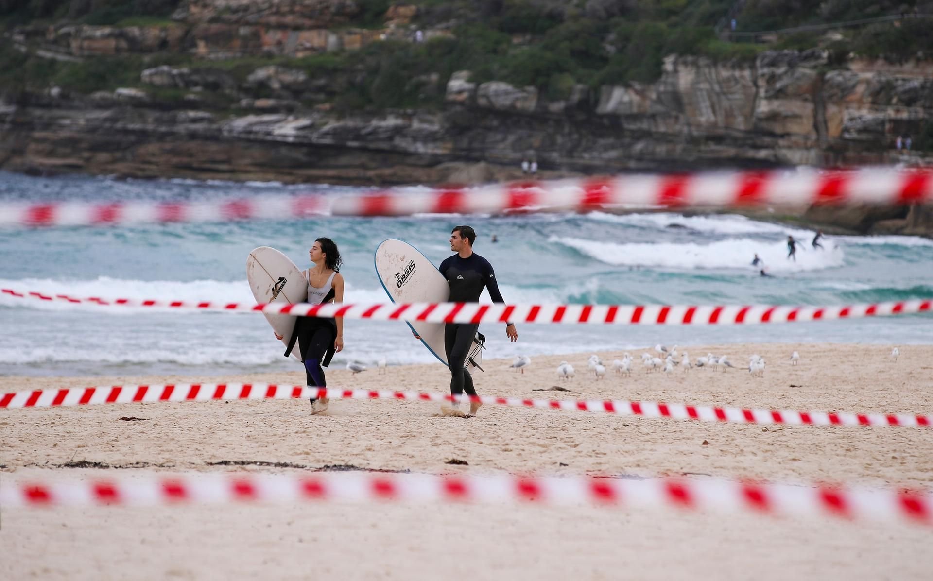 Zwei Surfer gehen hinter Absperrbändern am Bondi Beach entlang. (Symbolbild)