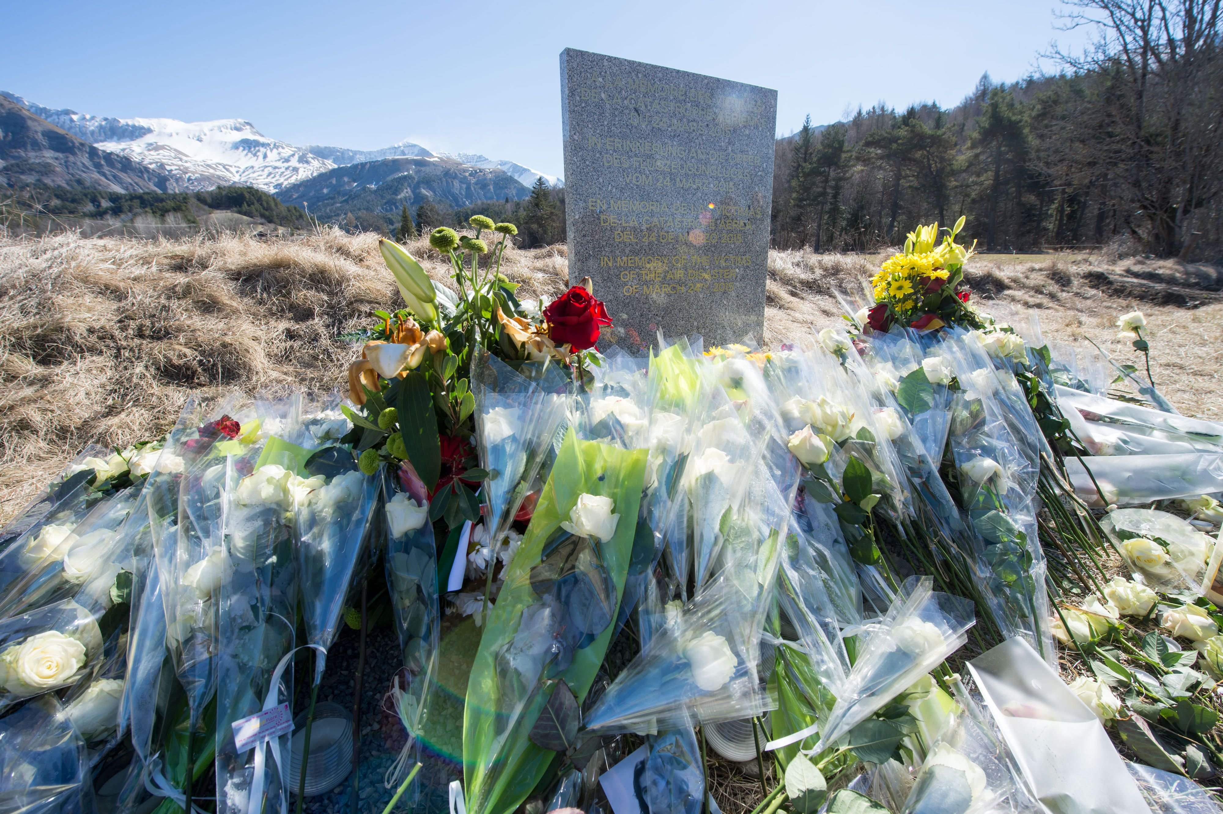 Inmitten von Blumen steht eine steinerne Gedenkstele mit der Aufschrift „In Erinnerung an die Opfer des Flugzeugunglücks vom 24. März 2015“ in Le Vernet.