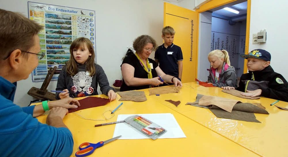 Museumspädagogin Susanne Wiermann schneidet für Konstantin das Leder aus, rechts daneben Emma und Janick, links Josefin.