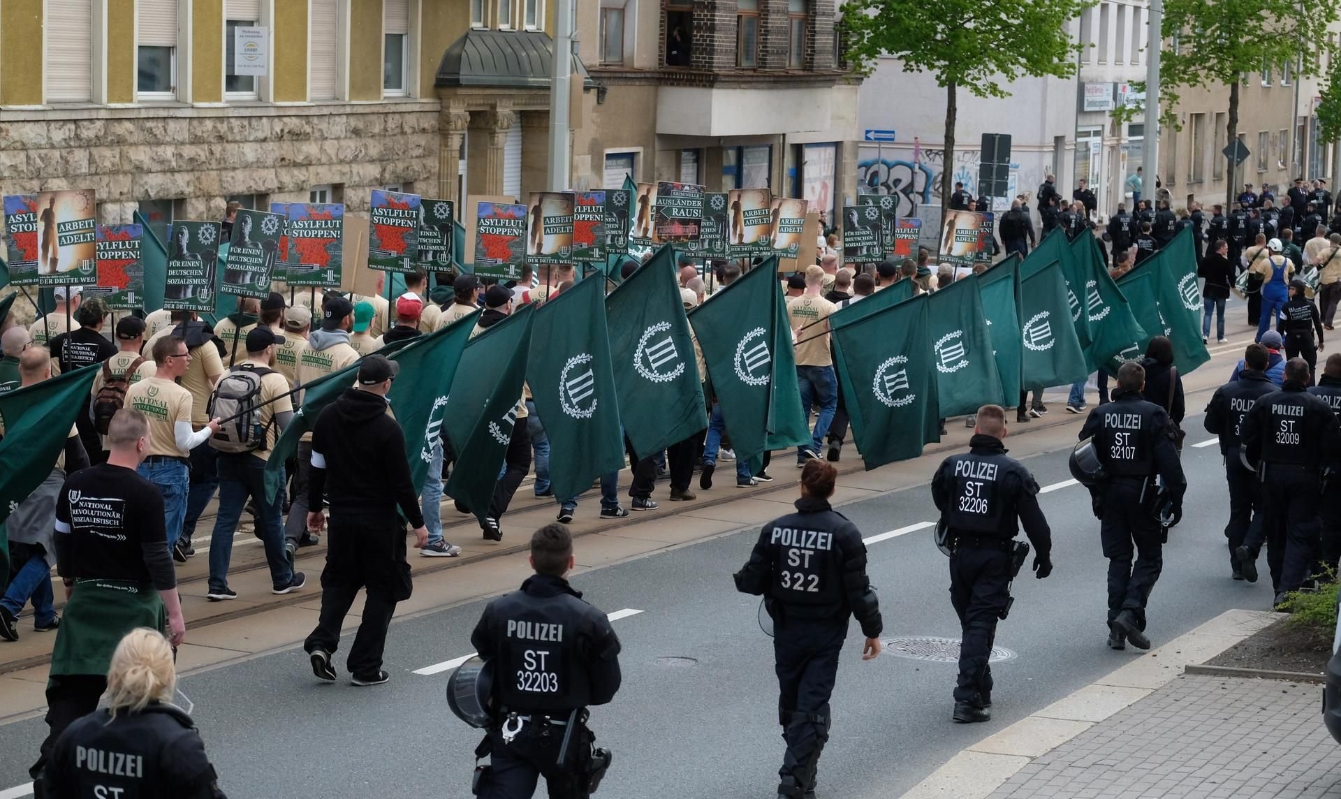Teilnehmer eines rechten Aufmarsches der Partei ·„Der III. Weg“ marschieren in Begleitung der Polizei in Plauen eine Straße entlang.