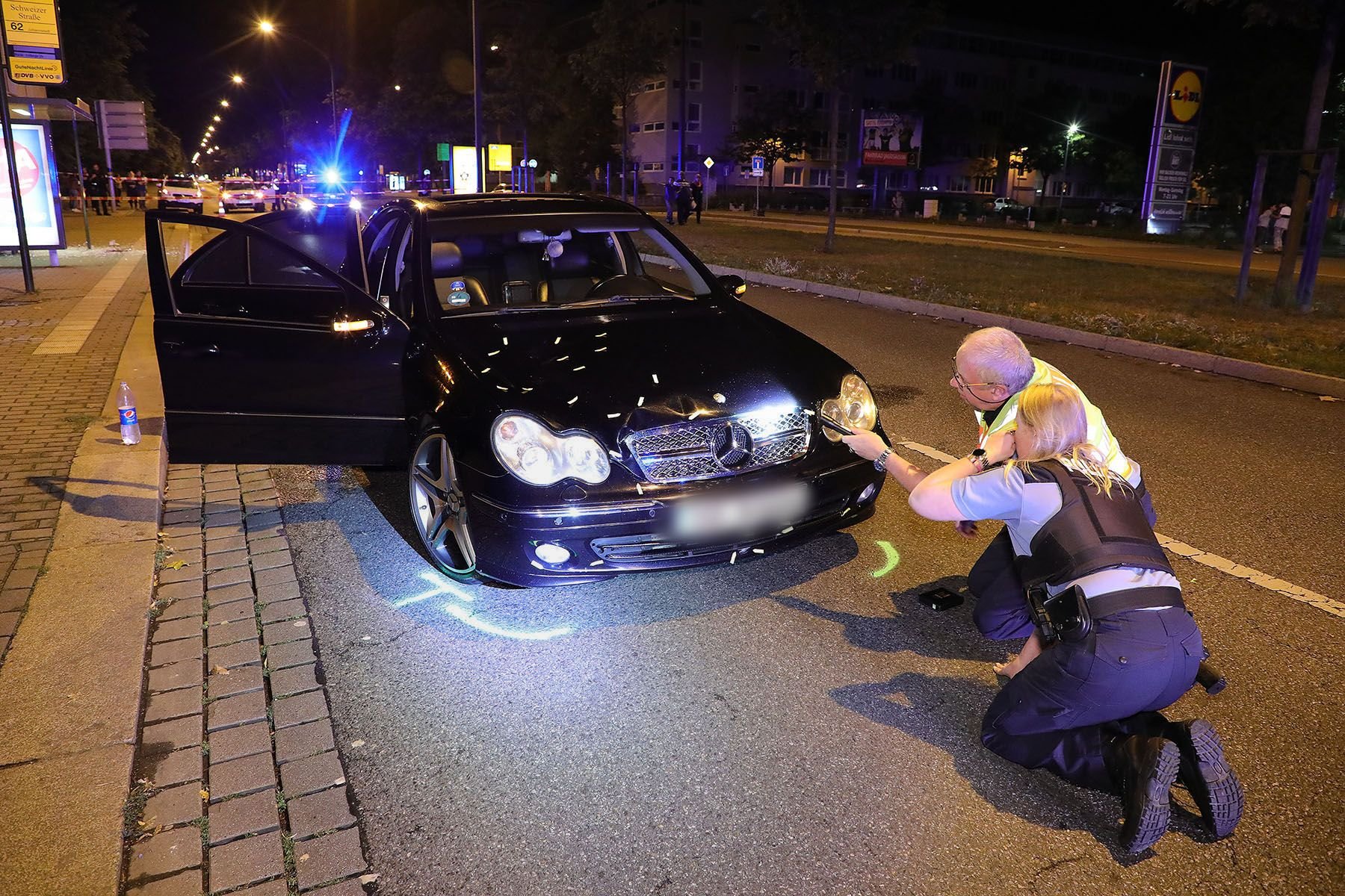 Dresden: Zwei Polizisten suchen auf einer abgesperrten Straße an einem schwarzen Mercedes, der in einen Verkehrsunfall verwickelt ist, mit einer Taschenlampe nach weiteren Spuren.