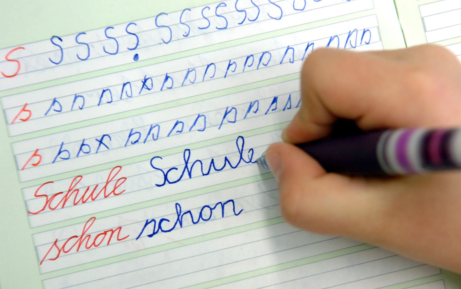 In einer Schule schreibt ein Mädchen im Unterricht das Wort „Schule“ in ihr Heft.