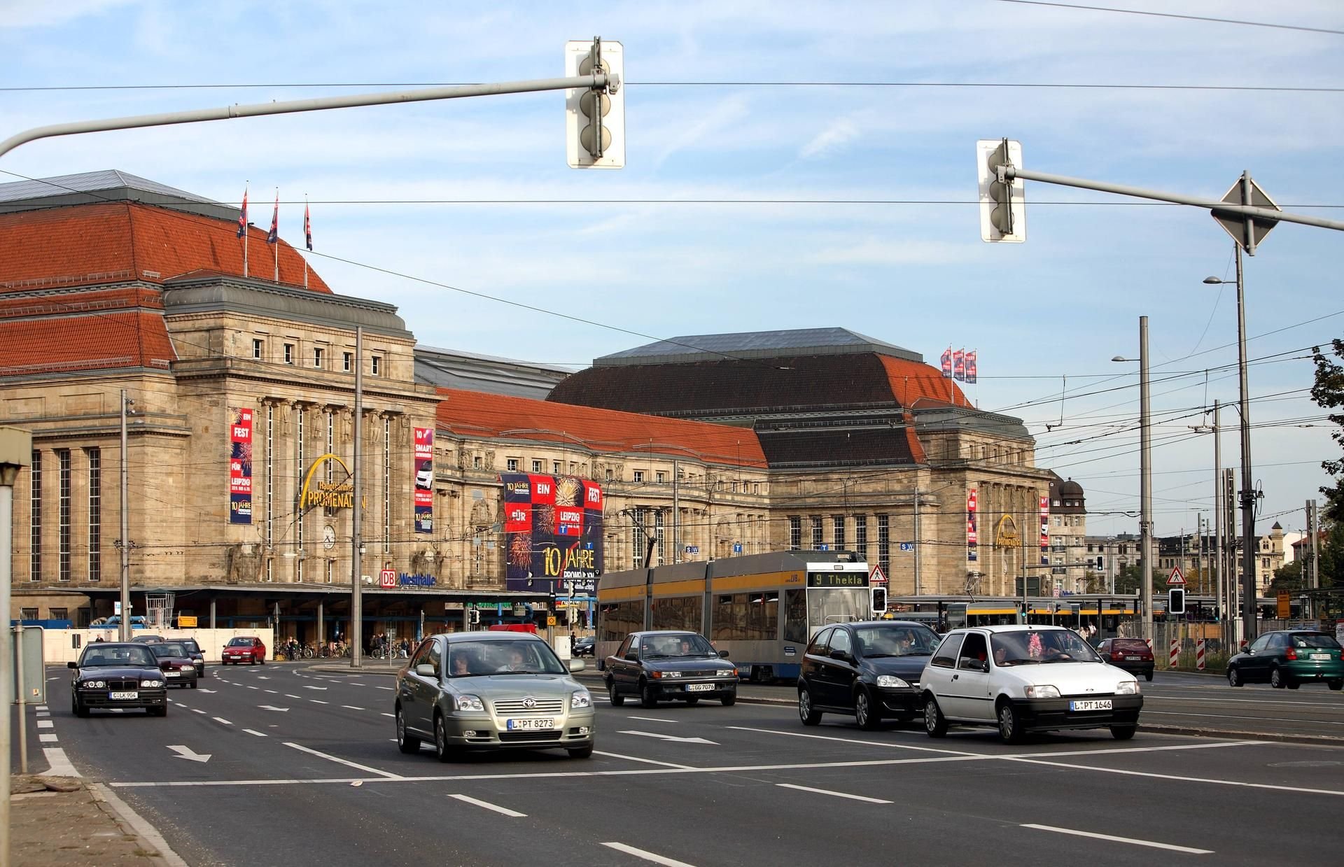 Autos und eine Straßenbahn der LVB fahren passieren die Straße am Haupteingang des Leipziger Hauptbahnhofs.