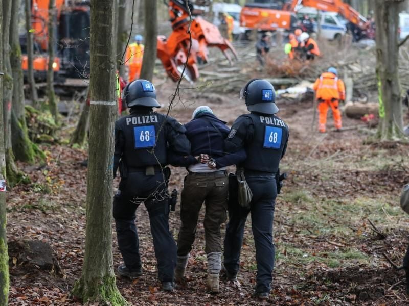 Polizisten führen eine A49-Gegnerin durch ein bereits gerodetes Waldgebiet. Foto: Nadine Weigel/dpa