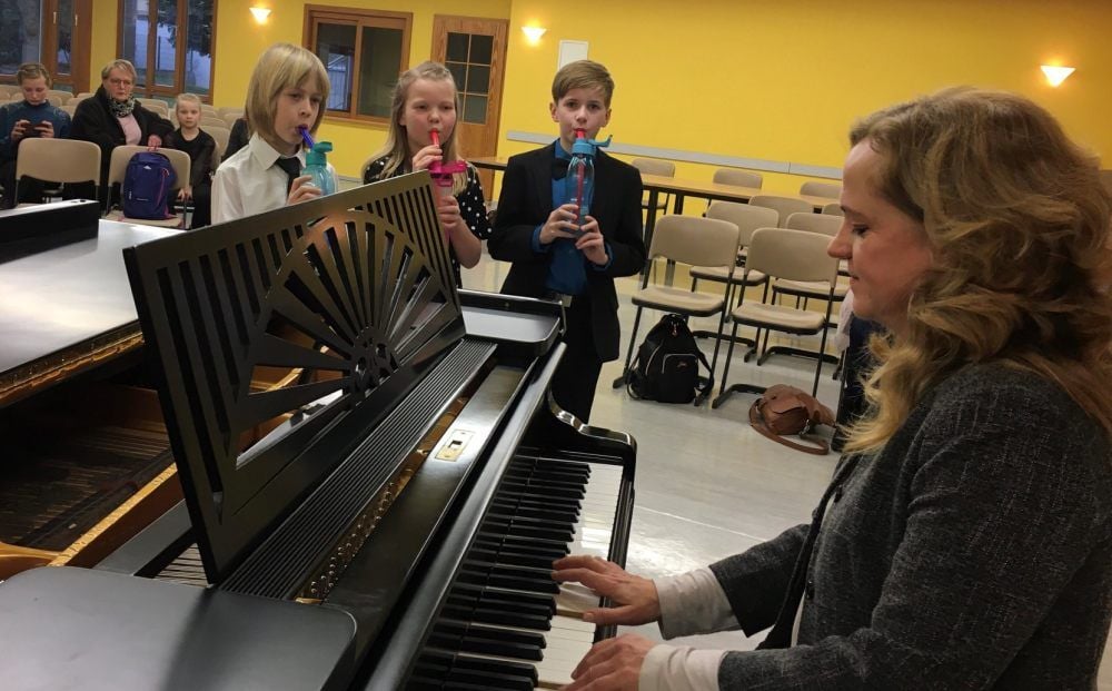 Einsingen mit Kristina Baran am Klavier: Maja Wünsche, Felix Keiner (weißes Hemd) und Otto Kiel (blaues Hemd) bei „Jugend musiziert“. Die Trinkbecher dienen der sogenannten Lax-vox-Methode für Stimmtraining.