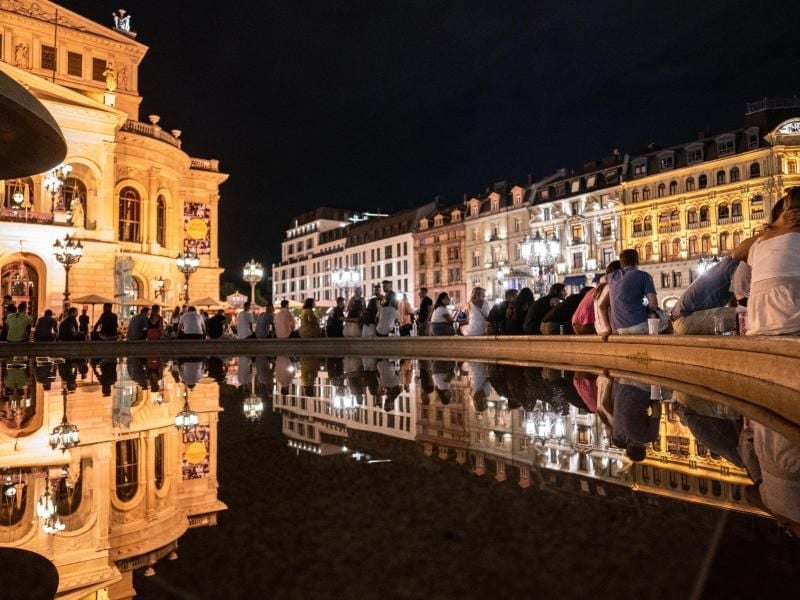 Menschen sitzen am Abend rund um den Brunnen vor der Alten Oper. Foto: Frank Rumpenhorst/dpa