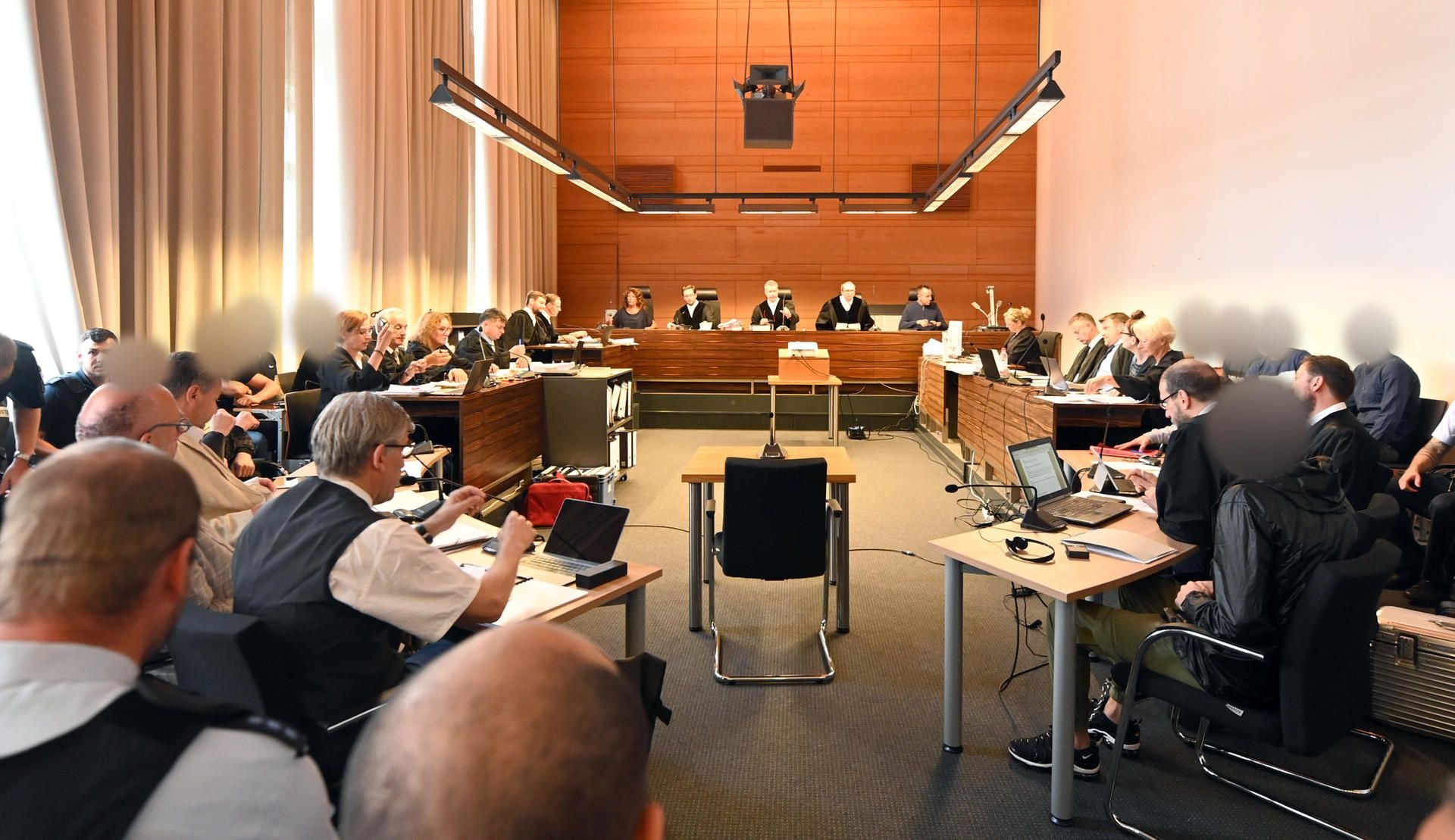 Die elf Angeklagten sitzen im August 2019 mit Justizbeamten im Landgericht seitlich hinter ihren Anwälten.
