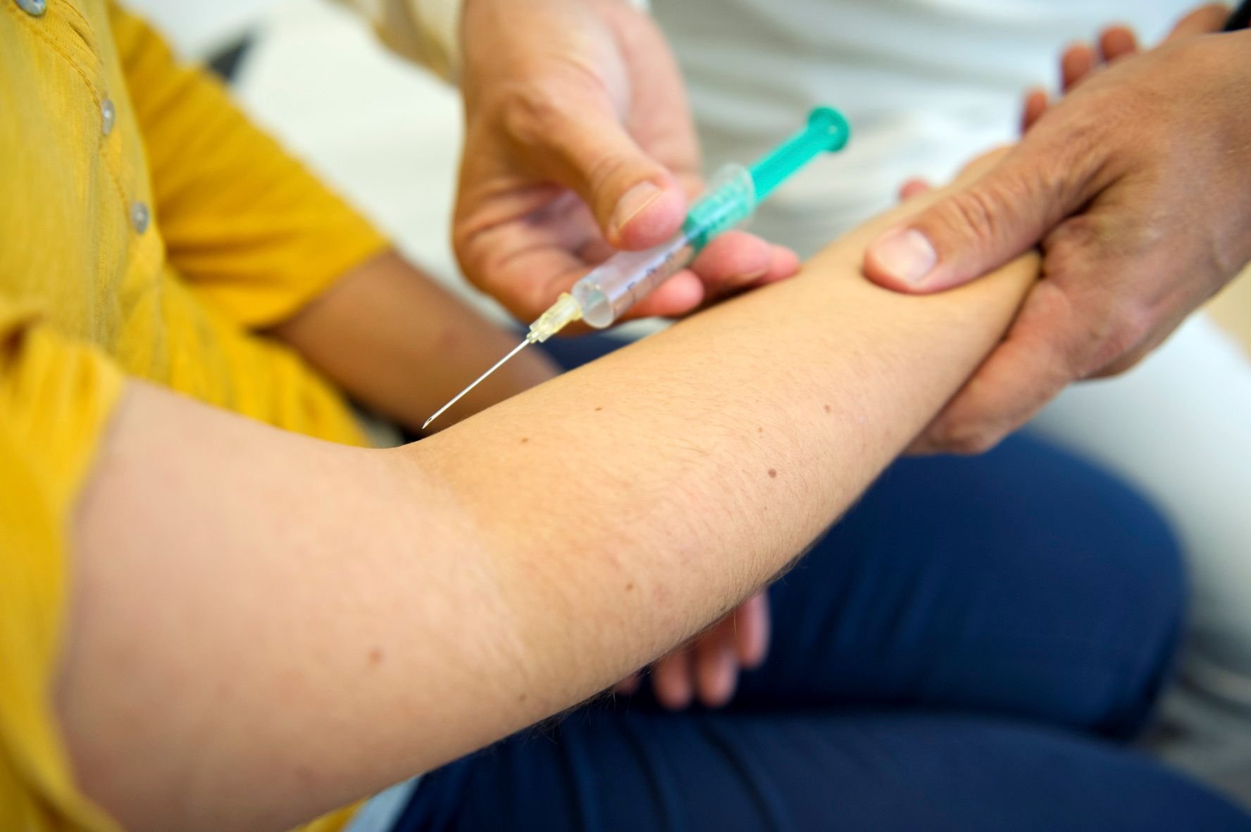 Ein Arzt setzt in einer Praxis eine Spritze am Arm eines Patienten an.