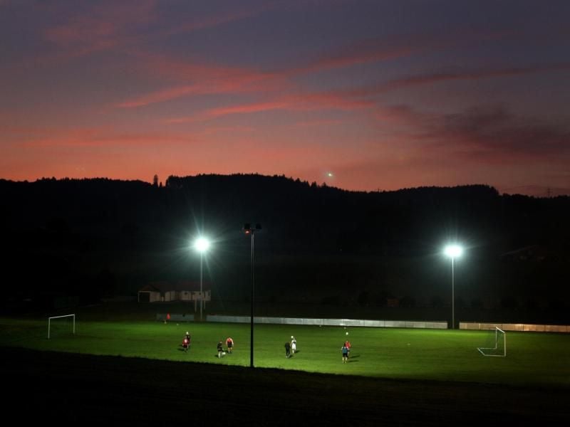Fußballspieler trainieren kurz nach Sonnenuntergang auf einem im Flutlicht liegenden Fußballplatz. Foto: Karl-Josef Hildenbrand/dpa