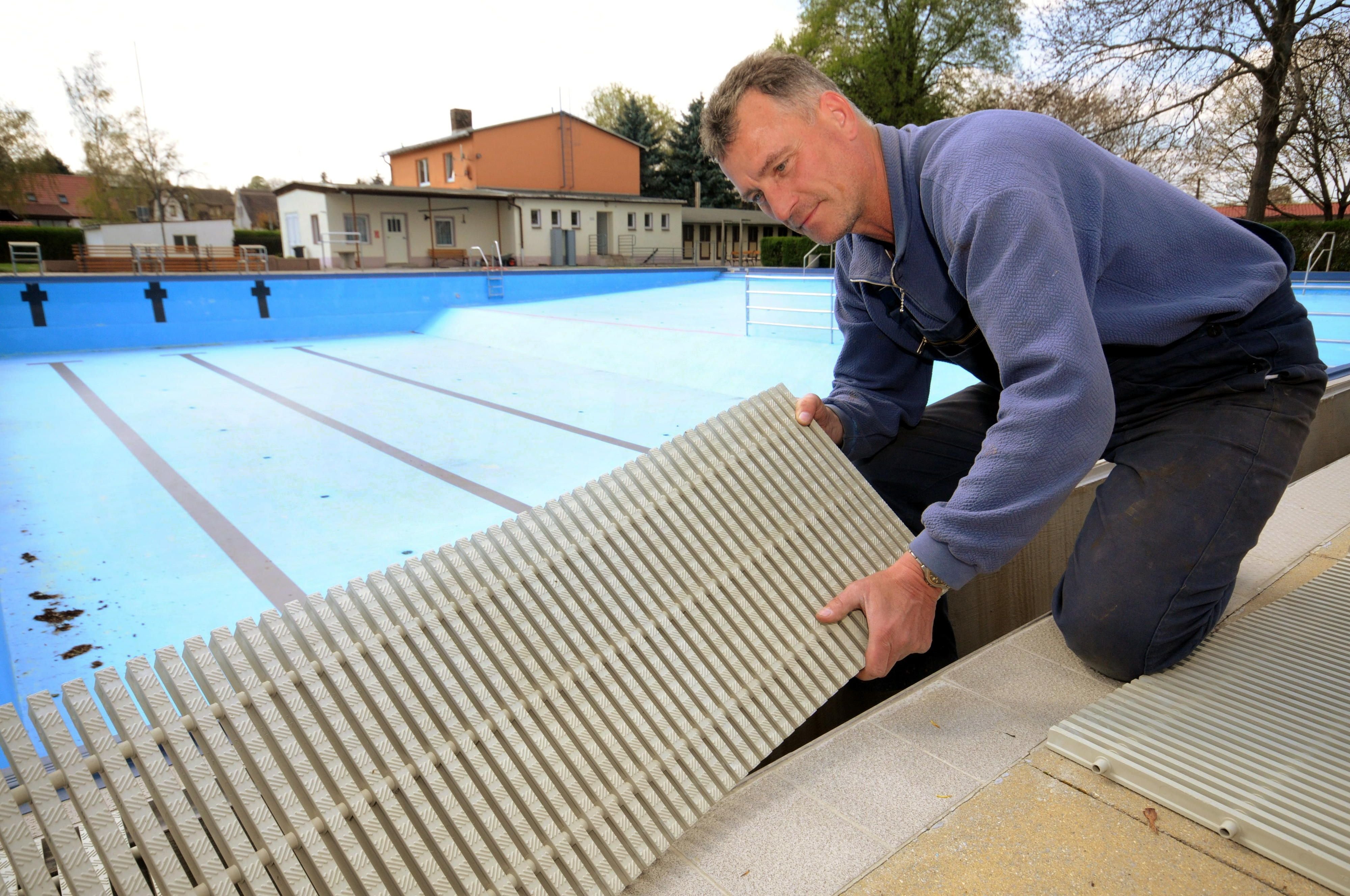 Schwimmmeister Fred Hänsel legt ein Andeckrost auf die Überlaufrinne des Schwimmbeckens in Alsleben.