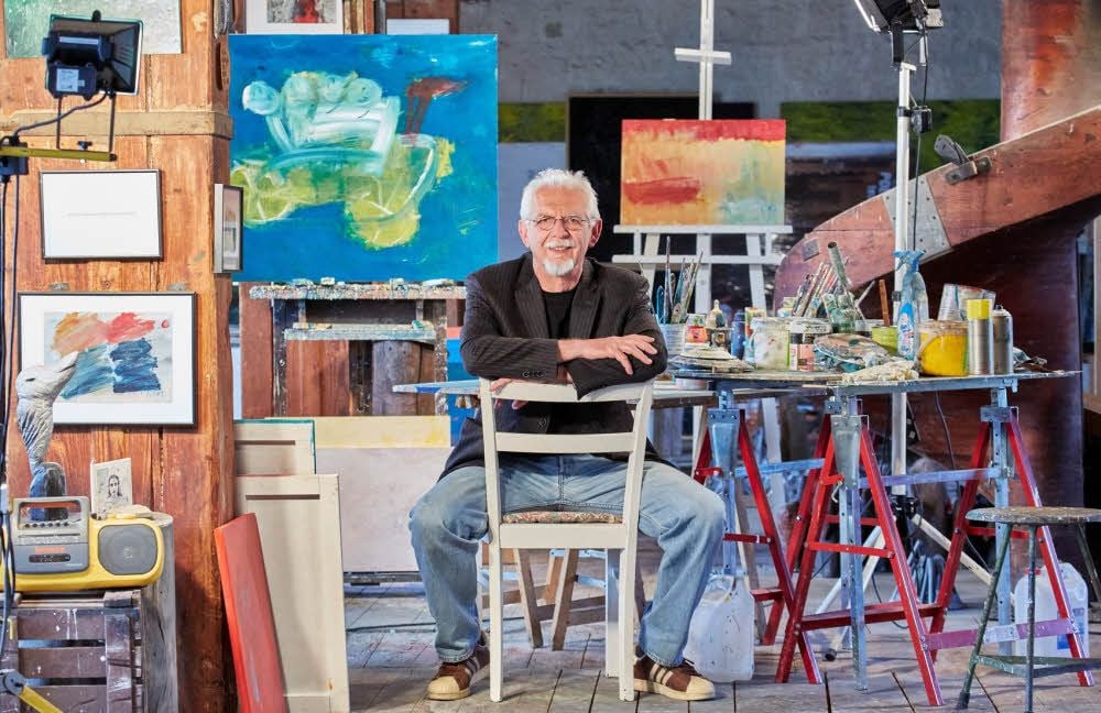 Ulrich Tarlatt in seinem Atelier in der Bernburger Saalemühle. Das Bild „Unterwegs, on the road“ (hinten links) ist Teil der aktuellen Schau.