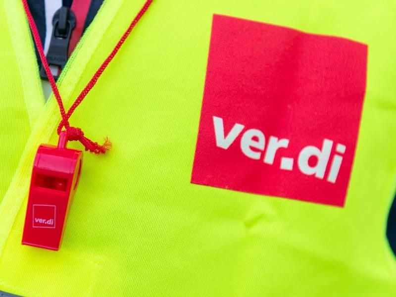 Ein Streikender trägt eine Warnweste mit dem Verdi-Logo und eine rote Trillerpfeife. Foto: Christophe Gateau/dpa