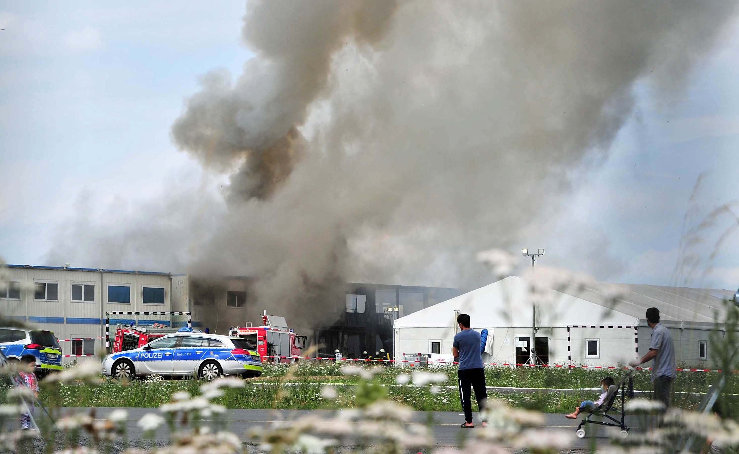 Flüchtlinge verfolgen die Löscharbeiten bei dem Brand in der Flüchtlingsunterkunft am alten Flughafen Kassel-Calden (Hessen).