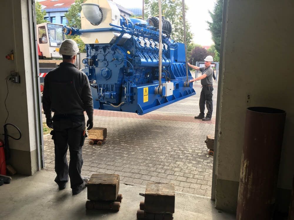 Langsam wird das Kraftwerk an das Tor zur KE-Halle gehoben, dort durch Mitarbeiter von Kruse-Montagen auf Rollen aufgesetzt und mittels Winde in die Halle hineingezogen. 600 Kilo Zugkraft reichen, um den Elf-Tonner zu bewegen.