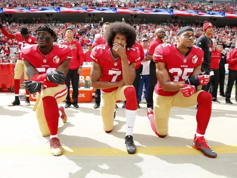 Colin Kaepernick (M), Eli Harold (l) und Eric Reid von den San Francisco 49ers knien 2016 beim Abspielen der US-Nationalhymne. Foto: John G Mabanglo/EPA/dpa