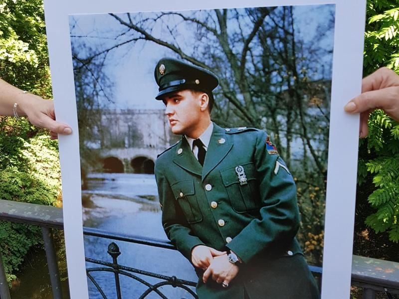 Zwei Personen halten auf einer Fußgängerbrücke in Bad Nauheim ein Foto von US-Sänger Elvis Presley hoch. Foto: Carolin Eckenfels/Archivbild
