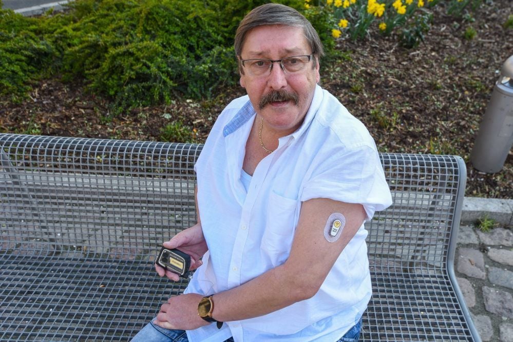Ralf Glaubel zeigt einen Chip an seinem Oberarm, der regelmäßig seinen Blutzuckerwert misst. Der Diabetiker kann den dann auf seinem Handy ablesen. Seine Erfahrung ist, dass man trotz Diabetes heute fast ohne Einschränkungen leben kann.