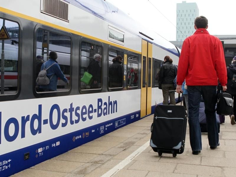 Passagiere gehen an einem Zug der Nord-Ostsee-Bahn entlang. Foto: Malte Christians/Archiv