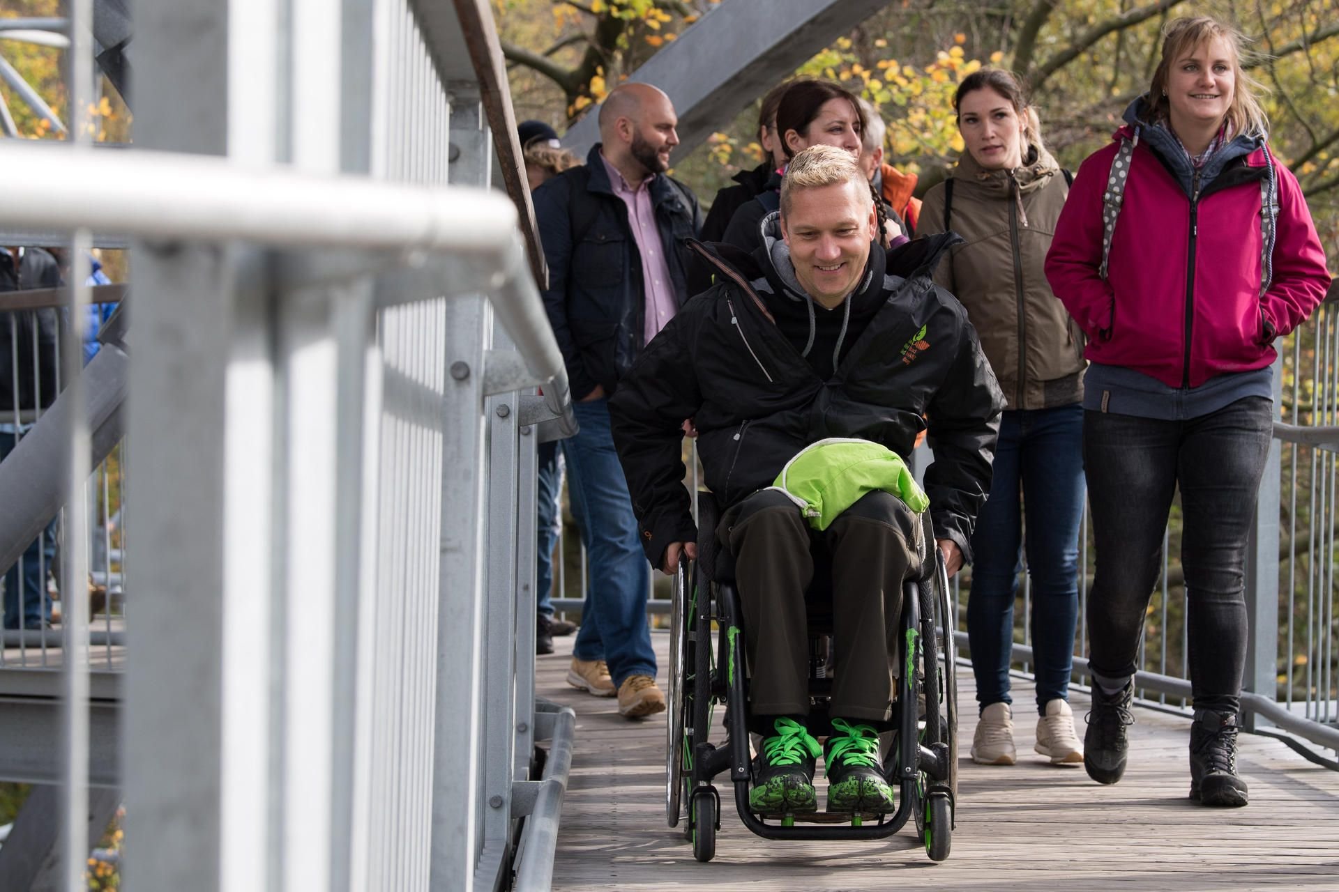 Rollstuhlguide Timo Kazcmarek rollt mit Besuchern zur Aussichtsplattform am Baumwipfelpfad Harz in Bad Harzburg