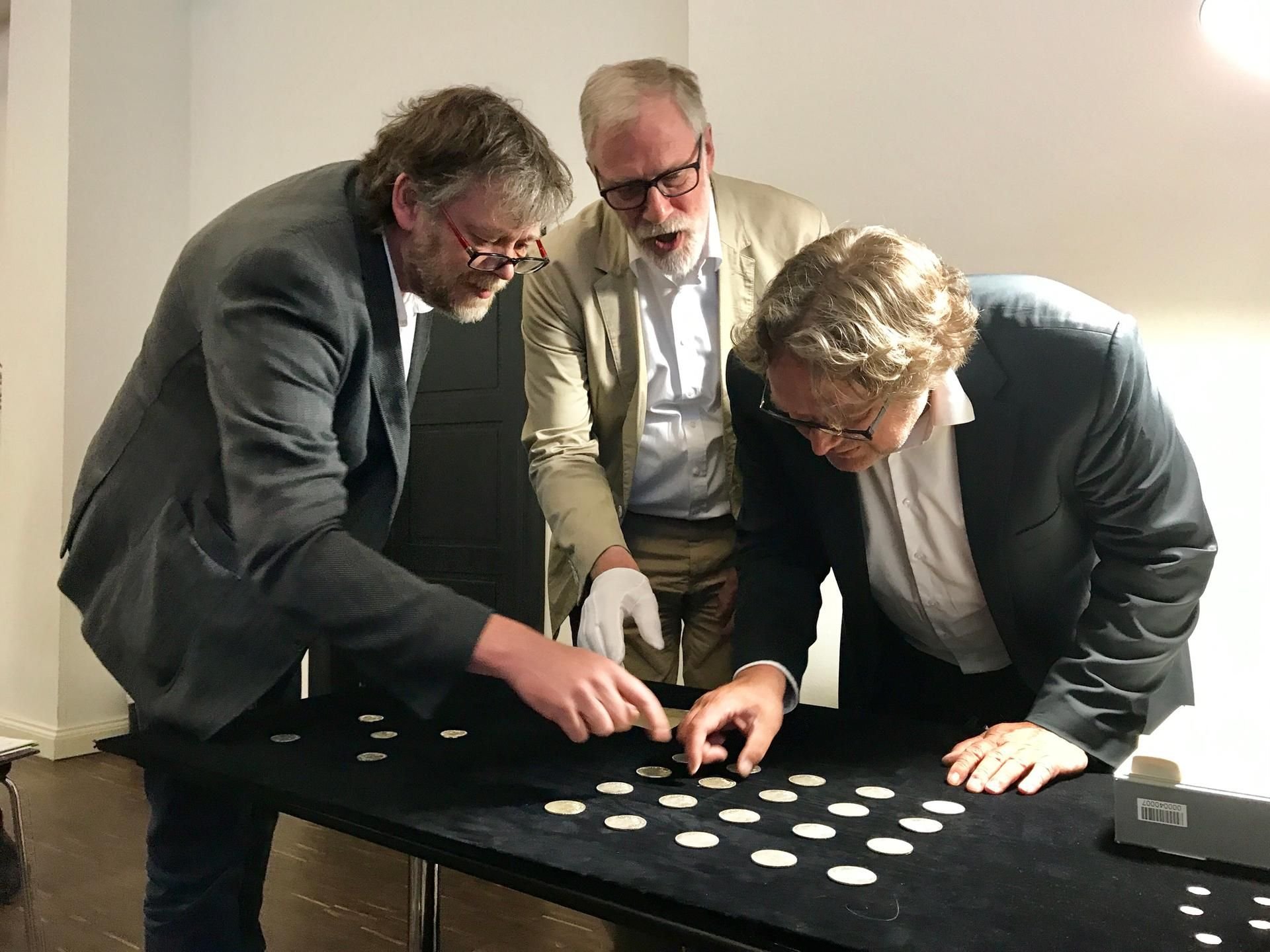 Münzexperte Ulf Dräger von der Moritzburg, Kulturminister Rainer Robra und Landesarchäologe Harald Meller (von links) begutachten im Landesmuseum für Vorgeschichte in Halle eine Auswahl von Münzen aus dem 11. bis 18. Jahrhundert. (Archivbild)
